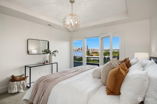 carpeted bedroom featuring a notable chandelier, a water view, access to outside, and a tray ceiling