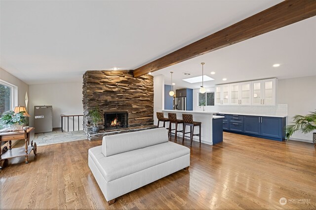 living room with lofted ceiling with beams, a stone fireplace, and light hardwood / wood-style flooring