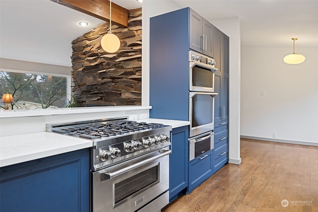 kitchen with decorative light fixtures, light wood-type flooring, appliances with stainless steel finishes, and blue cabinetry