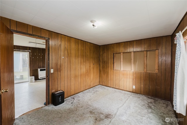 empty room with light colored carpet, heating unit, and wood walls