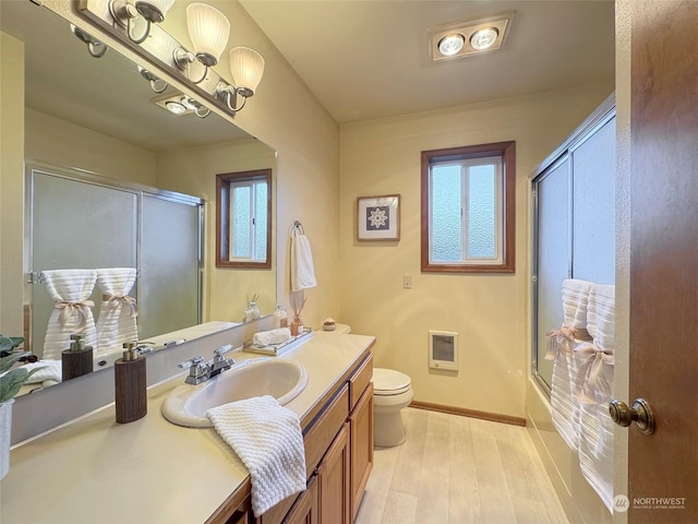 full bathroom with toilet, heating unit, vanity, enclosed tub / shower combo, and hardwood / wood-style floors