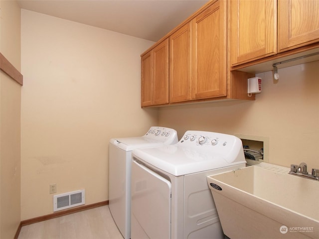 clothes washing area with separate washer and dryer, sink, and cabinets