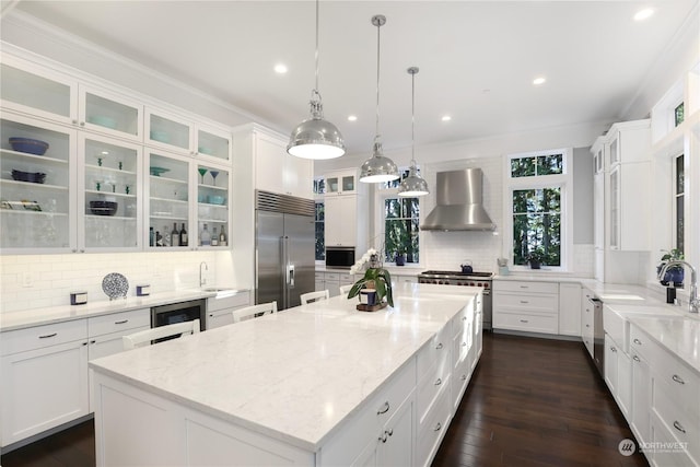 kitchen featuring stainless steel appliances, a center island, light stone countertops, white cabinetry, and wall chimney range hood