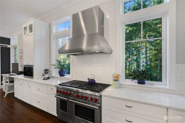 kitchen with light stone countertops, range with two ovens, ornamental molding, white cabinetry, and extractor fan