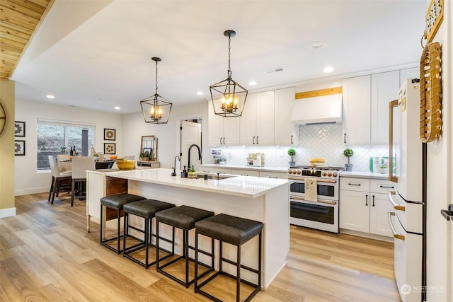 kitchen featuring extractor fan, sink, white cabinets, double oven range, and a kitchen island with sink