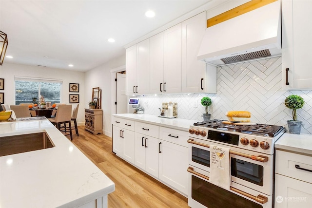 kitchen with tasteful backsplash, double oven range, custom exhaust hood, and white cabinets