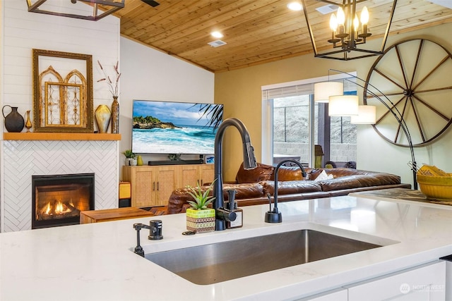 kitchen featuring lofted ceiling, sink, wood ceiling, a tile fireplace, and decorative light fixtures