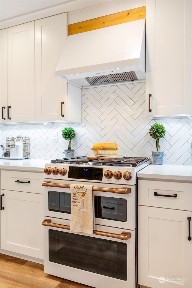 kitchen with tasteful backsplash, double oven range, premium range hood, and white cabinetry