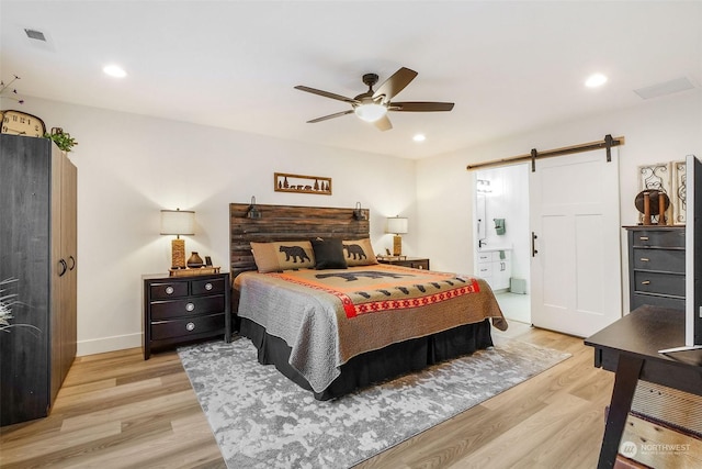 bedroom featuring a barn door, light hardwood / wood-style flooring, ceiling fan, and ensuite bath