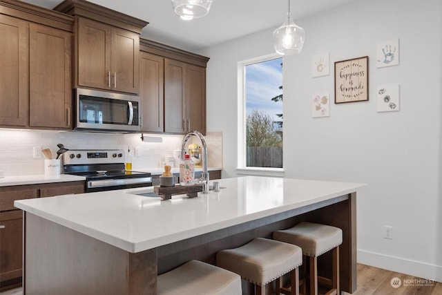 kitchen with sink, appliances with stainless steel finishes, a kitchen island with sink, and decorative backsplash