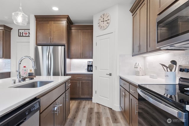 kitchen with light hardwood / wood-style floors, stainless steel appliances, decorative backsplash, sink, and decorative light fixtures