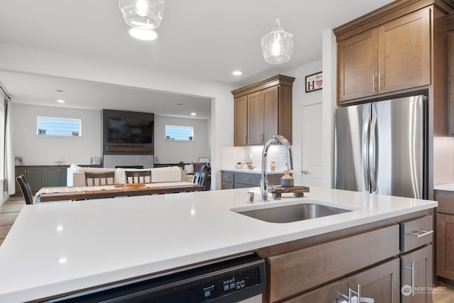 kitchen with sink, tasteful backsplash, an island with sink, hanging light fixtures, and stainless steel fridge