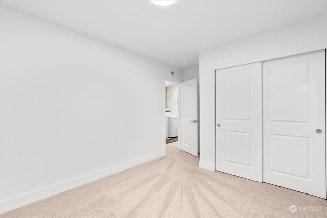 unfurnished bedroom featuring washer / clothes dryer, a closet, and light carpet