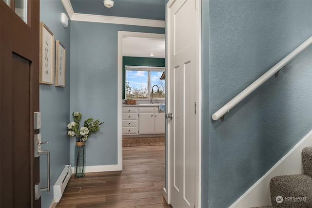 interior space with baseboard heating, ornamental molding, hardwood / wood-style flooring, and sink