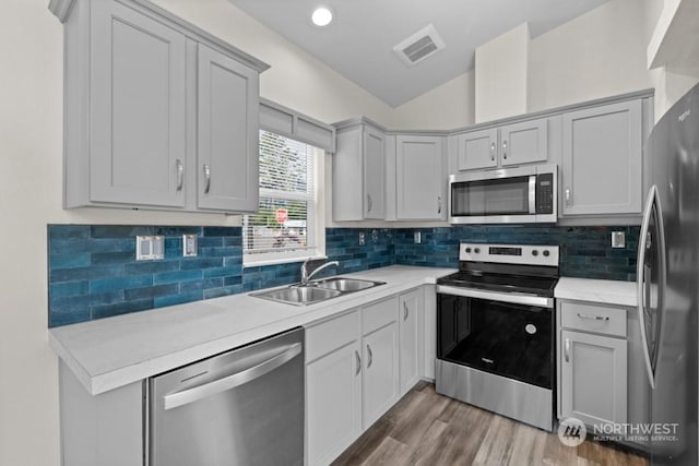 kitchen featuring sink, wood-type flooring, appliances with stainless steel finishes, gray cabinets, and backsplash