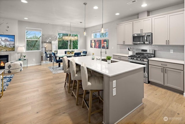 kitchen with a kitchen island with sink, sink, decorative light fixtures, light hardwood / wood-style flooring, and stainless steel appliances