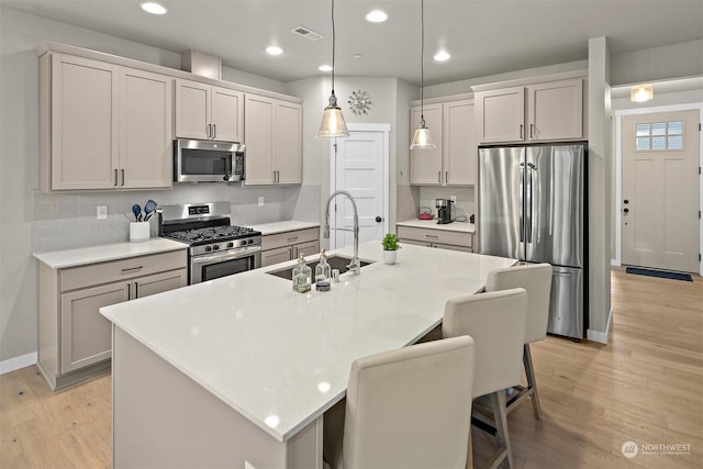 kitchen with pendant lighting, appliances with stainless steel finishes, an island with sink, sink, and a breakfast bar area