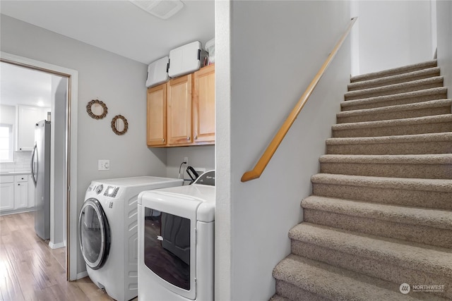 laundry room featuring light hardwood / wood-style floors, cabinets, and washing machine and dryer