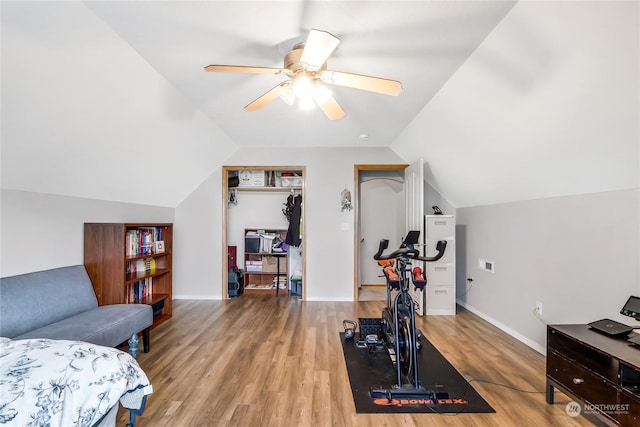 exercise room with ceiling fan, vaulted ceiling, and light wood-type flooring