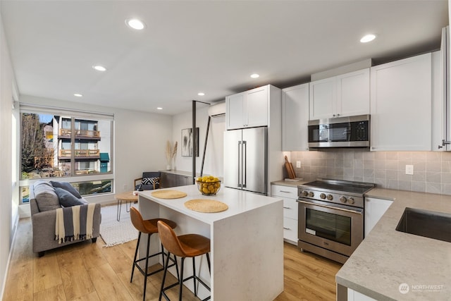 kitchen featuring premium appliances, white cabinets, a center island, decorative backsplash, and light hardwood / wood-style floors