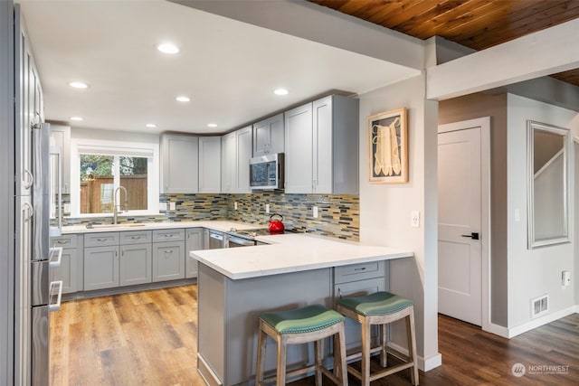 kitchen with a kitchen breakfast bar, appliances with stainless steel finishes, kitchen peninsula, sink, and tasteful backsplash