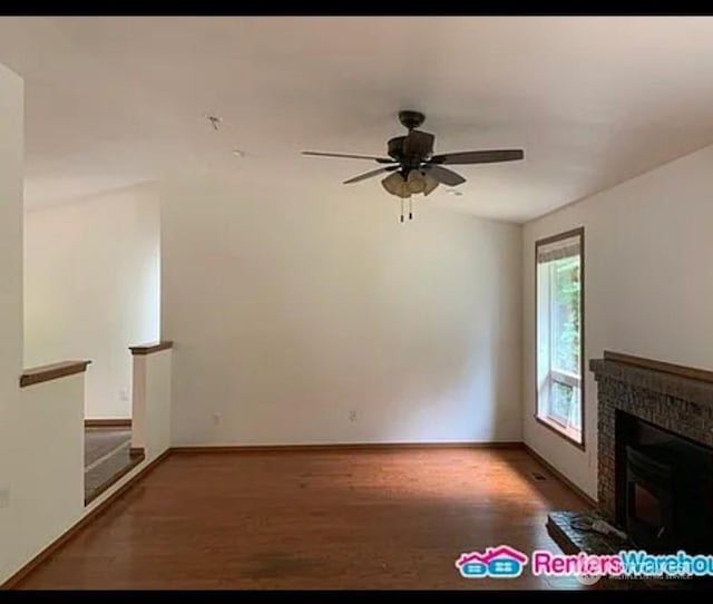 unfurnished living room with a tiled fireplace, ceiling fan, and dark wood-type flooring