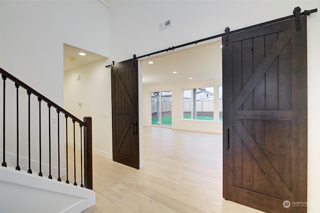 foyer entrance with a high ceiling, a barn door, and light hardwood / wood-style flooring