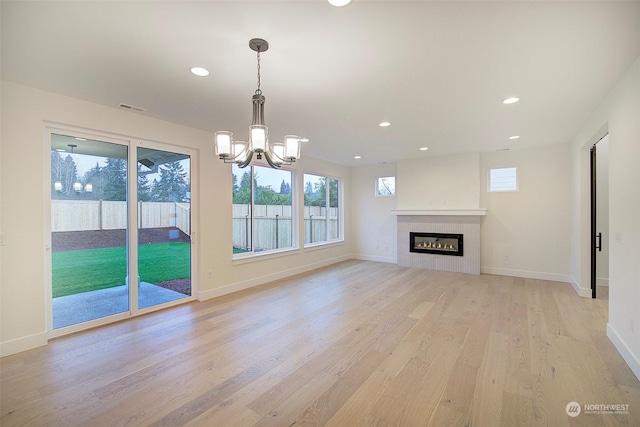 unfurnished living room with a tiled fireplace, light hardwood / wood-style flooring, and a notable chandelier