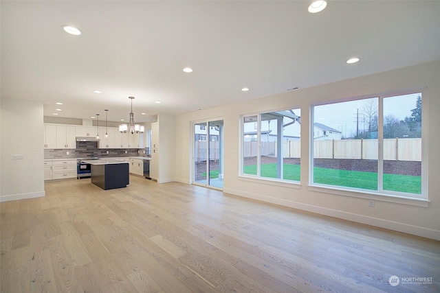 unfurnished living room featuring light wood-type flooring, an inviting chandelier, and plenty of natural light