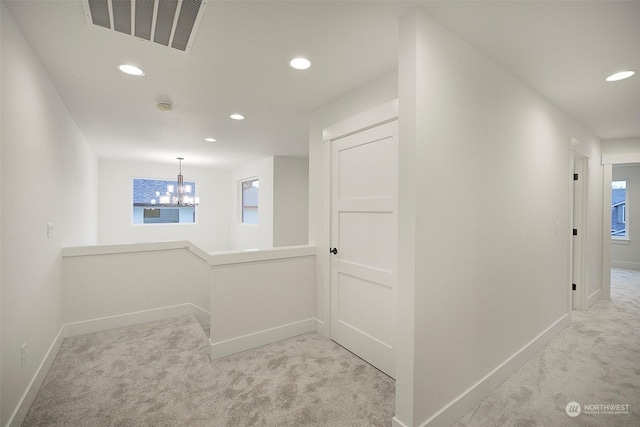 corridor with a wealth of natural light, light colored carpet, and a notable chandelier