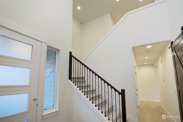 staircase with a high ceiling, wood-type flooring, a wealth of natural light, and a barn door