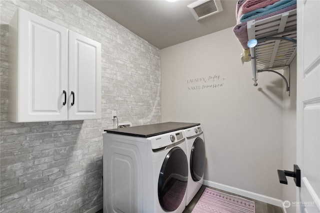 washroom featuring brick wall, separate washer and dryer, and cabinets