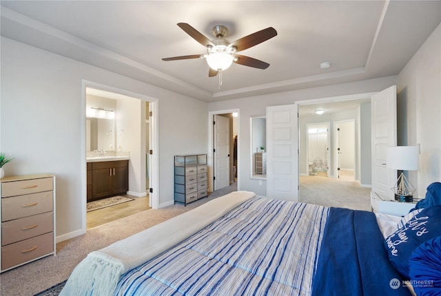 bedroom with a raised ceiling, ceiling fan, light colored carpet, and ensuite bath