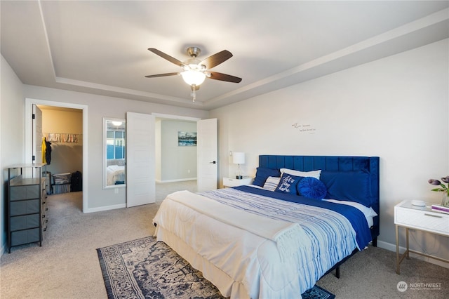 carpeted bedroom featuring ceiling fan, a walk in closet, and a raised ceiling