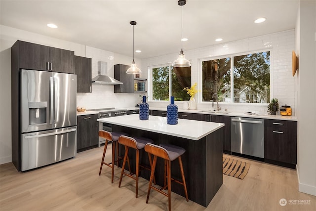 kitchen with wall chimney range hood, a kitchen island, sink, appliances with stainless steel finishes, and dark brown cabinets