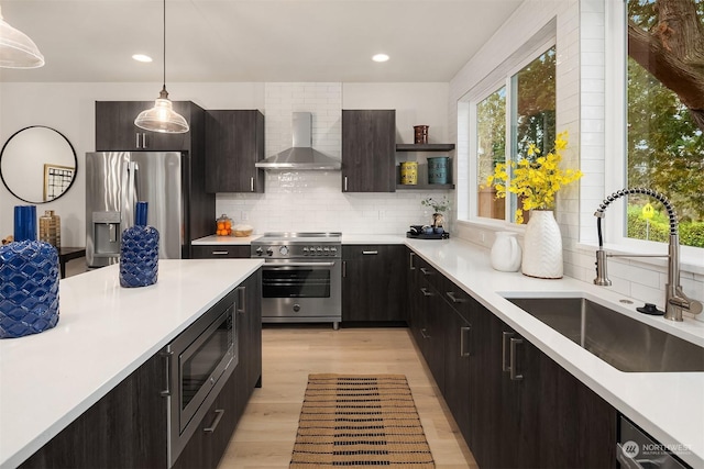 kitchen with appliances with stainless steel finishes, decorative backsplash, hanging light fixtures, wall chimney exhaust hood, and sink