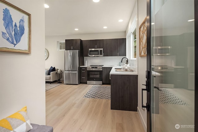 kitchen featuring backsplash, sink, dark brown cabinetry, light wood-type flooring, and appliances with stainless steel finishes