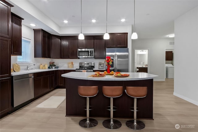 kitchen with sink, decorative light fixtures, dark brown cabinets, a kitchen island, and appliances with stainless steel finishes