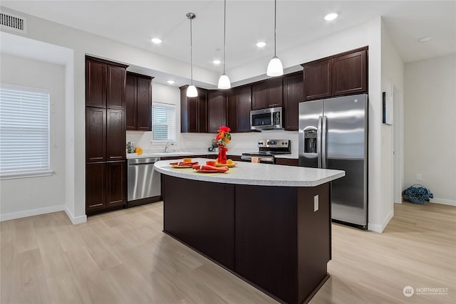 kitchen featuring hanging light fixtures, light hardwood / wood-style floors, a kitchen island, appliances with stainless steel finishes, and dark brown cabinetry