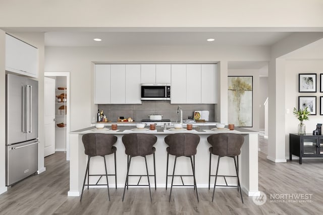 kitchen with white cabinets, stainless steel appliances, tasteful backsplash, light hardwood / wood-style flooring, and a breakfast bar area