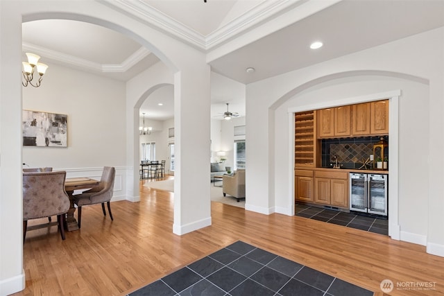 bar featuring wine cooler, ornamental molding, decorative backsplash, dark wood-style floors, and an inviting chandelier