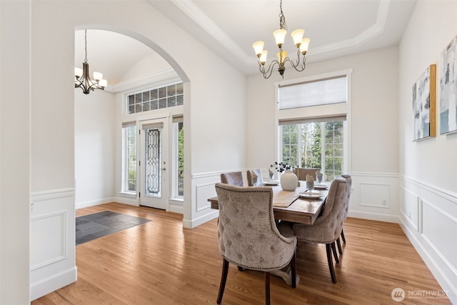 dining room featuring arched walkways, light wood-style floors, a raised ceiling, and a notable chandelier