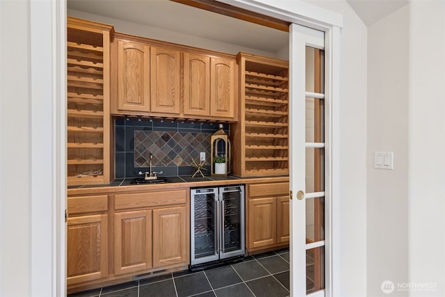 bar featuring wine cooler, decorative backsplash, wet bar, a sink, and dark tile patterned flooring