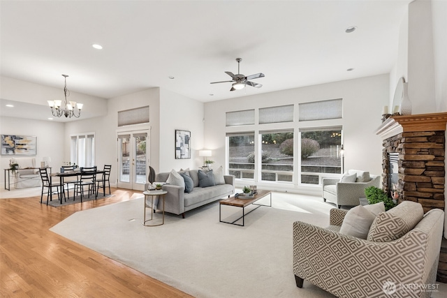 living area featuring french doors, wood finished floors, ceiling fan with notable chandelier, a stone fireplace, and recessed lighting