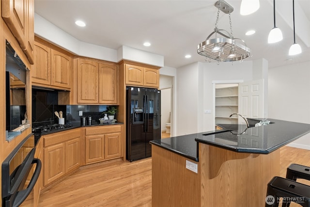 kitchen featuring light wood-style floors, a breakfast bar, dark stone countertops, black appliances, and pendant lighting