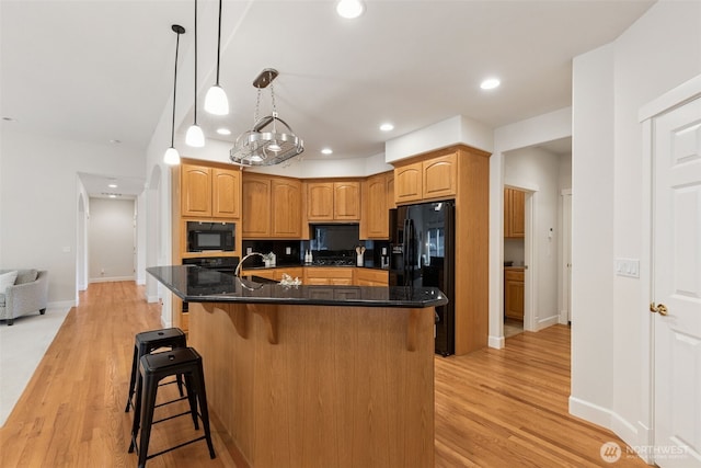 kitchen with a breakfast bar, black appliances, light wood finished floors, and recessed lighting