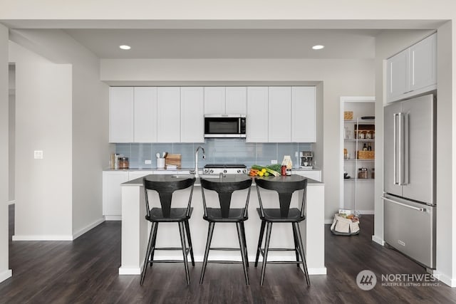 kitchen featuring white cabinets, appliances with stainless steel finishes, a breakfast bar area, and an island with sink