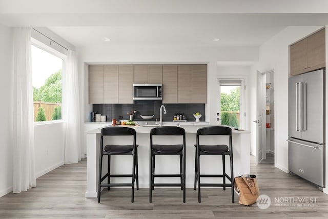 kitchen with tasteful backsplash, a breakfast bar, a kitchen island with sink, and stainless steel appliances