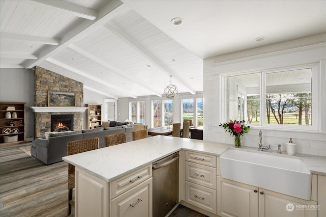 kitchen with kitchen peninsula, hardwood / wood-style floors, a fireplace, stainless steel dishwasher, and sink