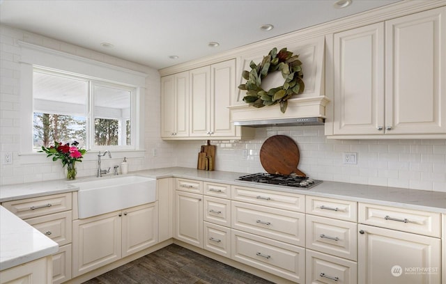 kitchen with backsplash, dark wood-type flooring, stainless steel gas cooktop, light stone counters, and sink